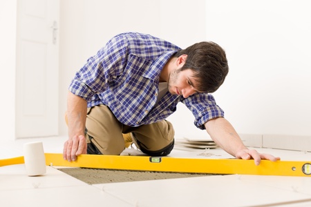 Home tile improvement - handyman with level laying down tile floorの写真素材