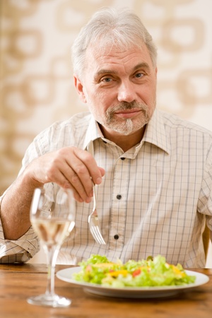Senior mature man eat vegetable salad and white wine at wooden tableの写真素材