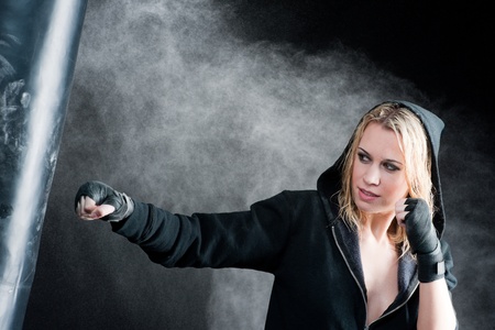Blond boxing woman in black training with punching bagの写真素材