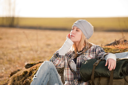 Camping young woman hiking with backpack sitting in countrysideの写真素材