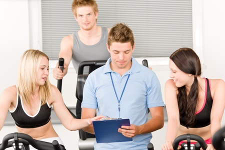 Young fitness instructor with gym people spinning or at cross-trainerの写真素材