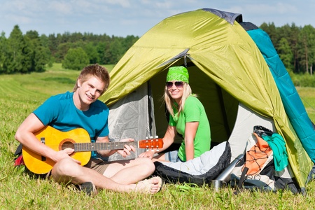 Happy camping couple sitting by tent play guitar sunny countrysideの写真素材