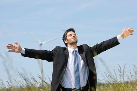 Green energy - Young businessman in field windmill in backgroundの写真素材