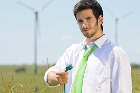 Green energy - young businessman hold plug in field with windmillの写真素材