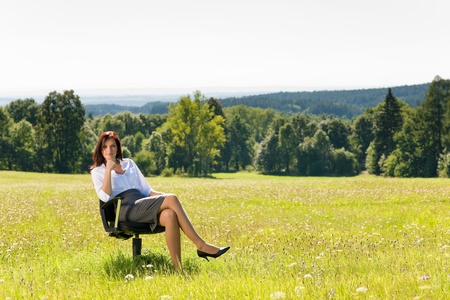 Young businesswoman sitting armchair outside in middle of sunny meadowの写真素材
