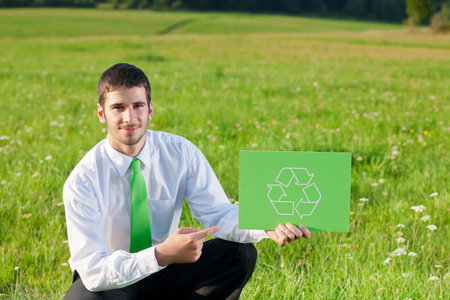 Green energy - Young businessman in sunny meadows hold recycling signの写真素材