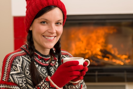 Winter christmas woman with hat and gloves drink by fireplaceの写真素材