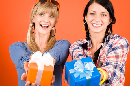 Two young woman friends hold party presents smiling orange backgroundの写真素材