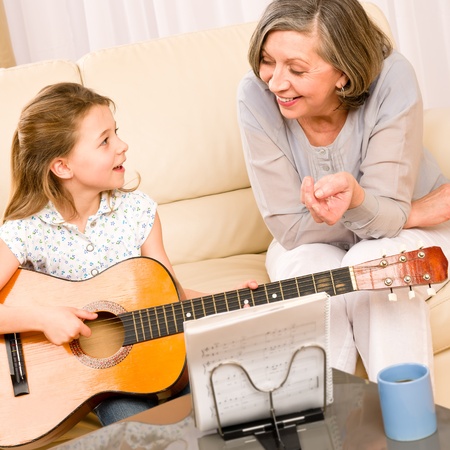 Young girl granddaughter sing play guitar to grandmother smileの写真素材