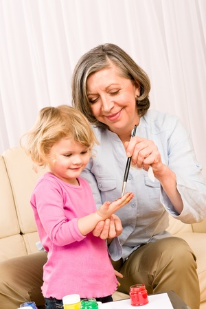 Grandmother with granddaughter playing together paint handprints on paperの写真素材