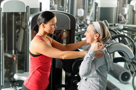 Fitness center senior woman exercise with personal trainer on machine