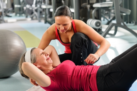 Fitness center senior woman exercise with personal trainer on matの写真素材