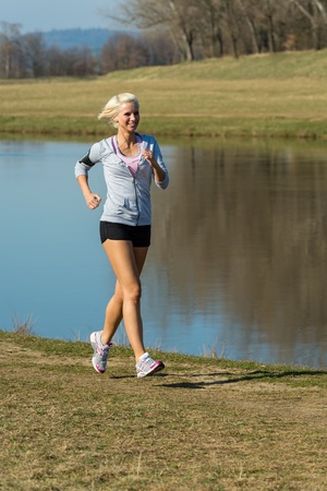 Running woman outdoor sport by river bank sunny dayの写真素材