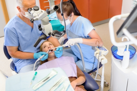 Dentist operating female patient through microscope at surgery officeの写真素材