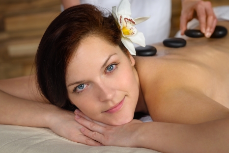 Woman with flower at spa having hot stone back treatmentの写真素材