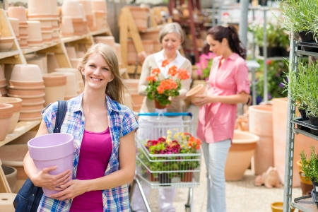 Smiling woman holding purple pot in garden store greenhouse centerの写真素材