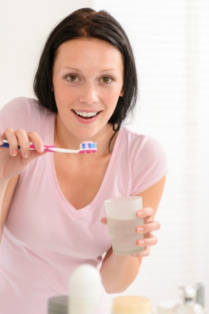 Young brunette woman brushing teeth with toothpaste holding glass waterの写真素材