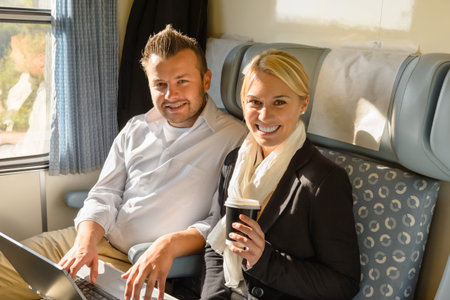 Woman and man sitting in train smiling laptop coffee commutersの写真素材