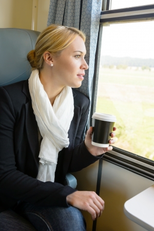 Woman looking out the train window pensive commuter coffee tripの写真素材