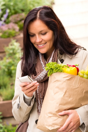 Smiling woman shopping vegetables mobile phone groceries messaging smsの写真素材
