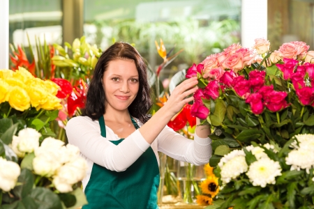 Happy young woman arranging flowers florist shop colorful rosesの写真素材