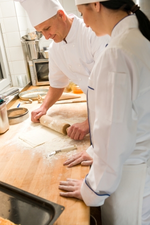 Male chef rolling dough with rolling pin assistant watchingの写真素材