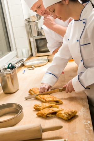 Female baker slicing strudel with male cook in kitchenの写真素材