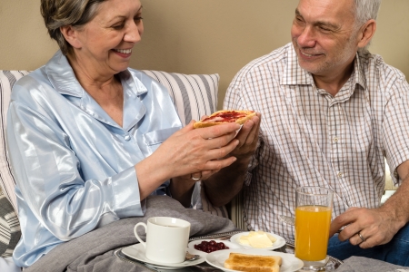 Senior couple having romantic morning breakfast in bedの写真素材