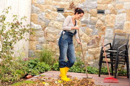 Young woman sweeping autumn leaves veranda backyard cleaning pileの写真素材