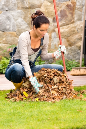 Young woman raking dry leaves pile backyard housework fallの写真素材
