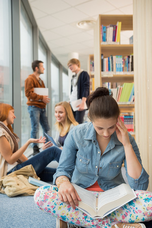 Girl reading book with group of students discussing in libraryの写真素材