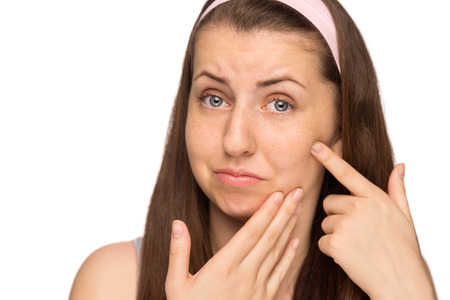 Unhappy girl squeezing pimple on cheek teenage beauty isolatedの写真素材