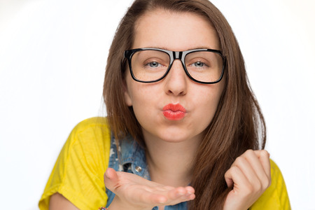Teenage girl in geek glasses blowing kiss on white backgroundの写真素材