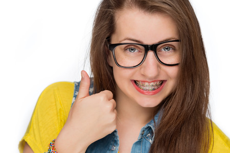 Girl with braces wearing geek glasses showing thumb up isolatedの写真素材