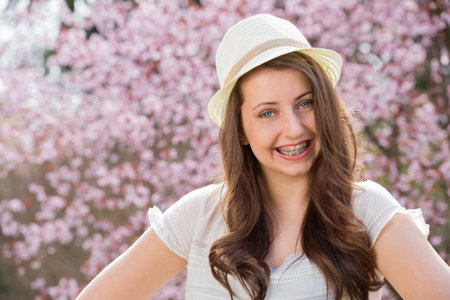 Girl with braces wearing hat in front of blossom tree