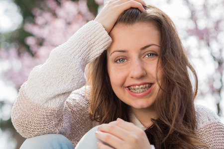 Happy girl wearing braces with hand in hair outdoors springの写真素材