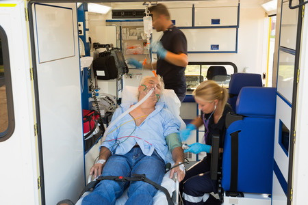 Paramedics treating unconscious elderly man on stretcher in ambulance carの写真素材