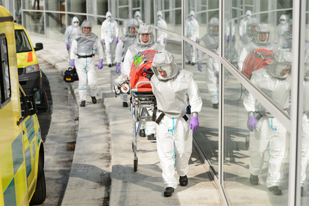 Biohazard team with stretcher wear protective uniform walking outside buildingの写真素材