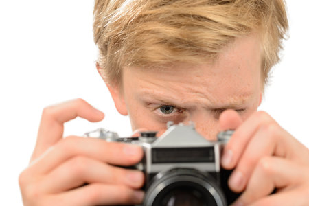 Teenage boy looking through retro camera photographing isolated on white