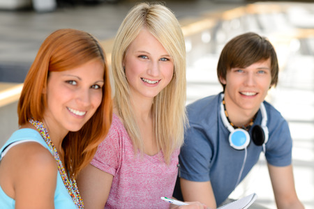 Three smiling college student friends sitting together looking at cameraの写真素材