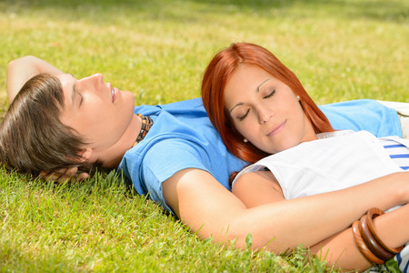 Teenage couple relaxing lying on grass closed eyes summer dayの写真素材