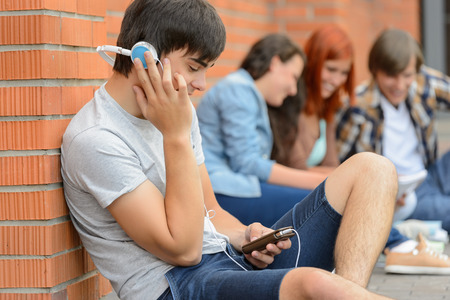 Student boy with headphones college friends sitting outside campus chattingの写真素材