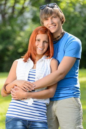 Romantic teenage couple hugging in sunny park smiling at cameraの写真素材