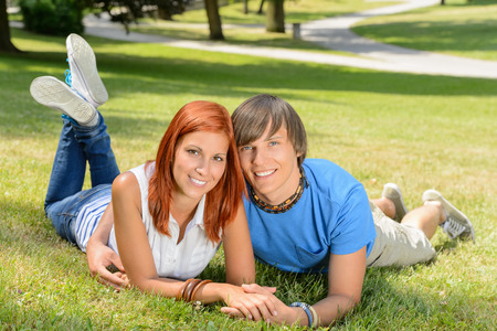 Smiling teenage couple lying in sunny park enjoy first loveの写真素材