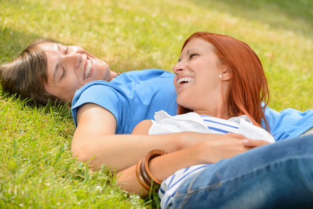 Cheerful teenage couple laughing at each other lying on grassの写真素材