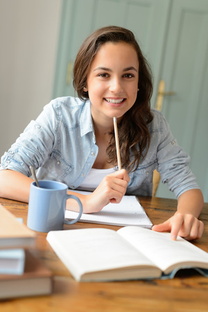 Student teenage girl studying at home sitting behind table smilingの写真素材