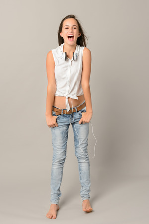 Singing teenage girl with headphones full length on grey backgroundの写真素材