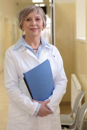 Senior doctor standing in hospital hallway holdings patient filesの写真素材
