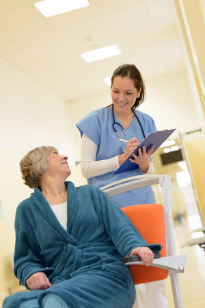 Smiling young female nurse watch senior patient in hospital while holding her filesの写真素材