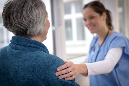 Smiling female nurse comforting senior patient in hospital corridorの写真素材